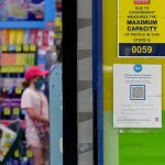 A sign outside a Chemist Warehouse says "COVID test currently sold out" as people queue in the background