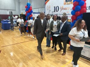 IMG_0074 - Caribbean Television Network Group of people at a career expo in a gym, walking past booths with red/blue balloons and a large 10 Years banner in the background.