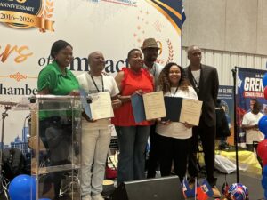 IMG_0081 - Caribbean Television Network Group of six award recipients on a stage, each holding certificates, smiling for a photo at a trade expo event.