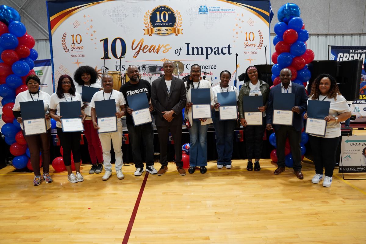 Group of people on a stage holding certificates at a 10-year anniversary event, with a banner reading '10 Years of Impact' in the background.