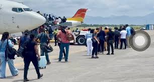Passengers stand in line on the tarmac near a white airplane with an orange and red tail, preparing to board a plane at the gate.