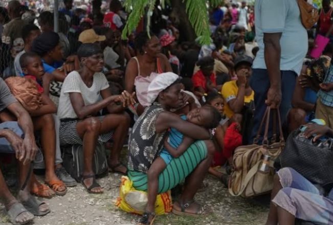 Crowded outdoor scene with a mother breastfeeding her baby while seated among a large group of people.