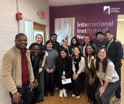 IINE - Caribbean Television Network Group of diverse students and staff posing for a photo in a hallway with a purple International Institute banner in the background.