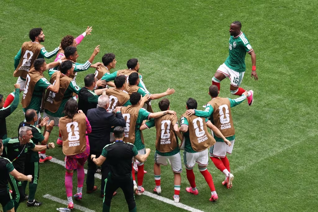 WhatsApp Image 2026-06-12 at 000047 - Caribbean Television Network Group of soccer players in green uniforms celebrate on a grass field, wearing brown bibs that say FIFA World Cup 2026, as they hug and cheer around one player stepping forward.