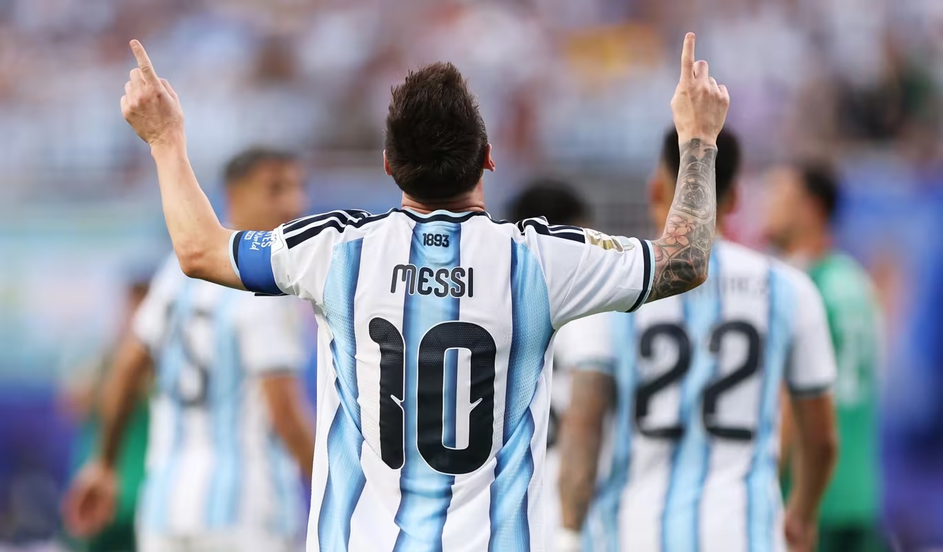 Back view of a soccer player in Argentina-style striped jersey with number 10, arms raised in celebration on the field.