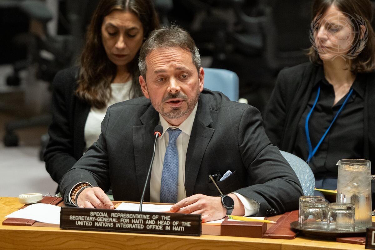 Senior UN official speaks into a microphone at a Haiti-focused meeting, seated at a desk with a formal nameplate in front.