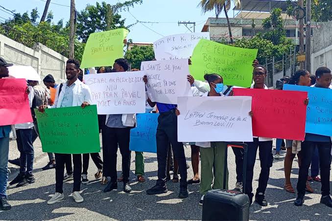 Group of young protesters holding colorful handwritten signs on a sunny street.
