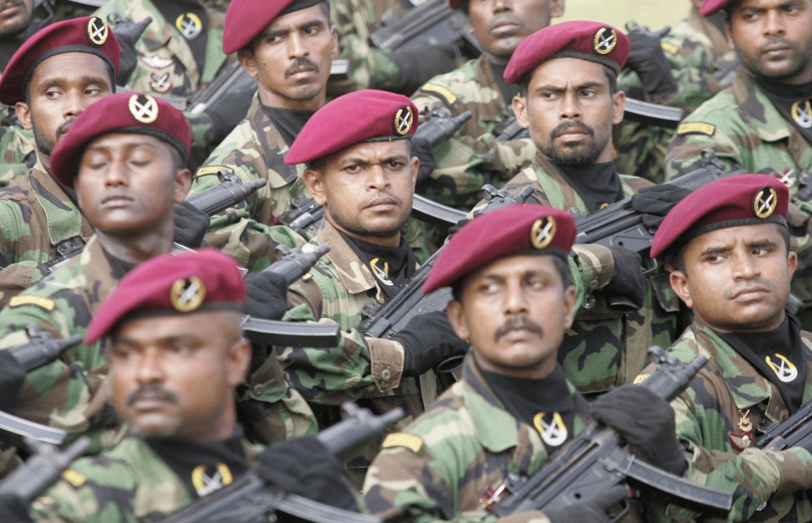 Group of soldiers in camouflage uniforms with maroon berets, holding rifles in formation.