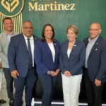 Group of professionally dressed adults posing for a photo in front of a green textured wall with a Martinez logo in the background.