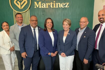Group of professionally dressed adults posing for a photo in front of a green textured wall with a Martinez logo in the background.
