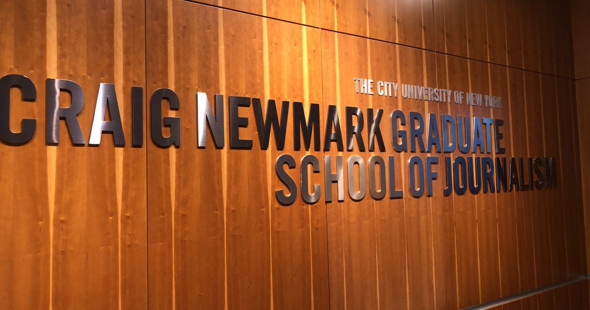 Wood-paneled wall with a large metallic sign reading 'CRAIG NEWMARK GRADUATE SCHOOL OF JOURNALISM' and a smaller 'The City University of New York'.