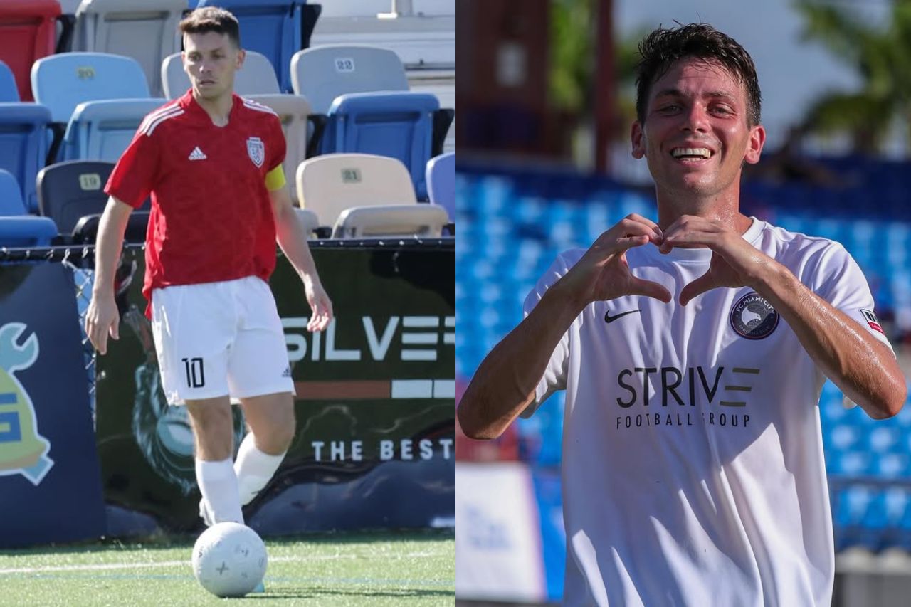 Soccer player in red jersey dribbles a ball on the field beside empty seats on the sideline.
