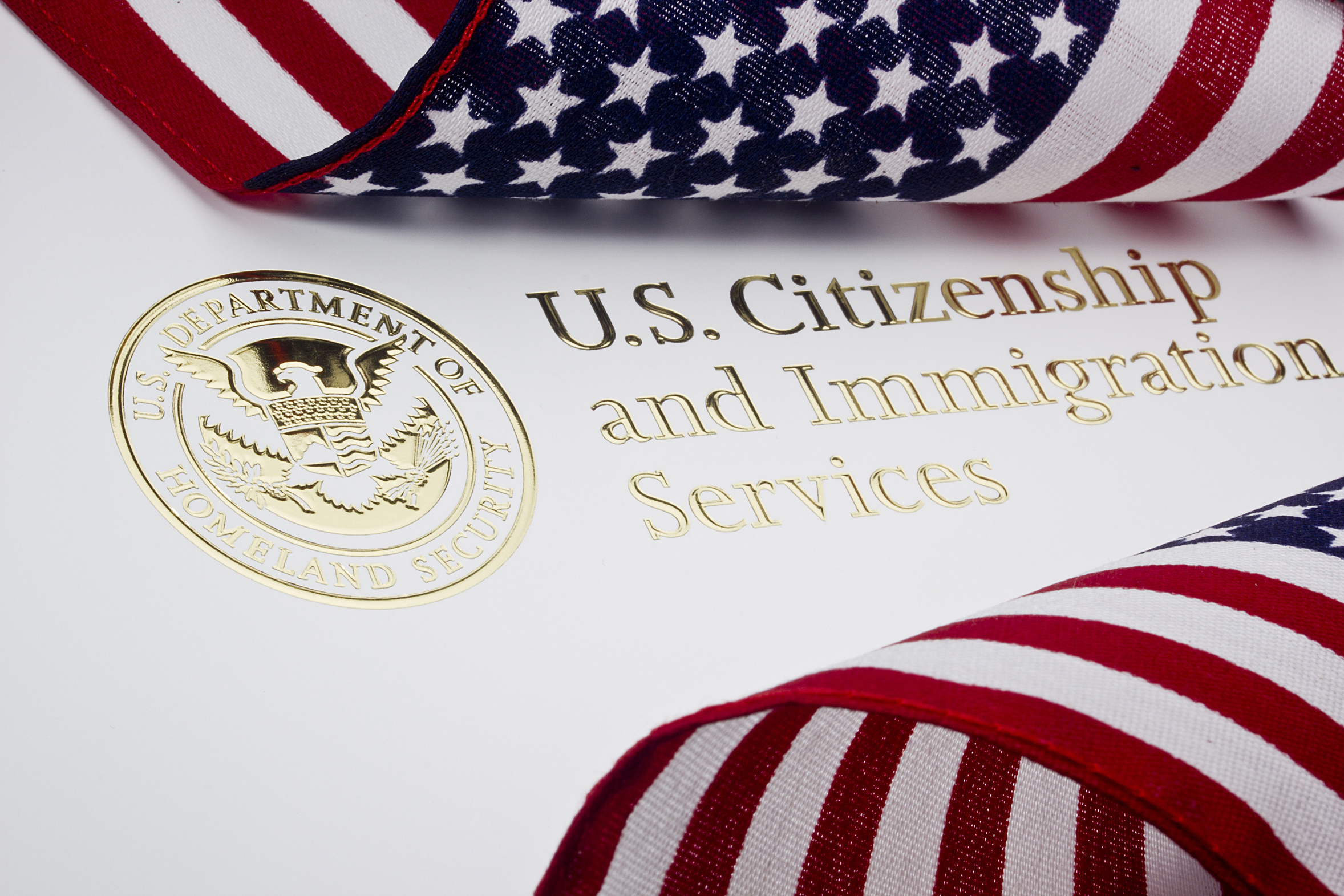 Close-up of US Citizenship and Immigration Services document with a gold seal, under a folded American flag ribbon